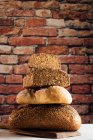 Pile de pain blanc et de seigle aux céréales et croûte appétissante sur planche à découper contre mur de briques dans la boulangerie — Photo de stock
