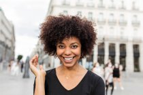 Молодая веселая афро-американка с прической афро, смотрящая в камеру на городской улице — стоковое фото