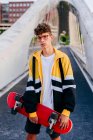 Caucasian teenager standing with a skateboard in the middle of the bridge in the city — Stock Photo