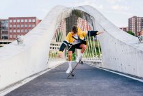 Caucasian teenager jumping with a skateboard in the middle of the bridge in the city — Stock Photo