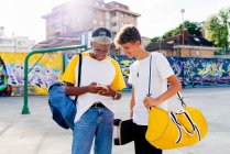 Двоє хлопчиків-підлітків зі скейтбордом та рюкзаком використовують телефон на вулиці — стокове фото