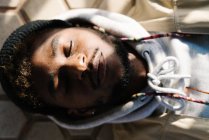 Visão superior da calma jovem barbudo afro-americano macho na roupa da moda deitado no chão com os olhos fechados no dia ensolarado — Fotografia de Stock