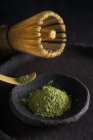 Cuillère avec feuilles de thé matcha séchées sur la vaisselle noire avec chasen pour la cérémonie orientale traditionnelle — Photo de stock