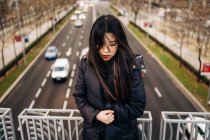 Lunghi capelli bruna donna asiatica in piedi su un ponte e guardando giù — Foto stock