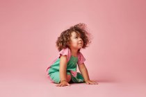 Criança adorável no vestido com cabelo encaracolado tendo uma birra olhando para longe inclinado sentado no chão — Fotografia de Stock