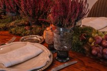 Alto ângulo de copos de cristal perto da placa e talheres colocados na mesa decorados com uvas Calluna vulgaris flores e romã — Fotografia de Stock