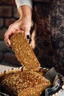 Crop anonymous female baker demonstrating soft fresh bread with crunchy seeds at table in bakery — Stock Photo