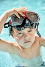 Adorable little boy in snorkeling goggles swimming in outdoor pool before diving training on sunny day — Stock Photo