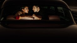Vista lateral do casal multiétnico sentado no banco de trás do auto antiquado — Fotografia de Stock