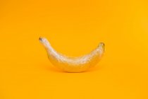 Deliziosa banana matura ricoperta di pellicola trasparente che rappresenta il concetto di agricoltura industriale su sfondo giallo brillante — Foto stock