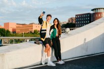 Couple of teenagers sitting on the wall and taking selfie with the phone in the street — Stock Photo