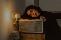 Ângulo alto de fêmea sonhadora apoiada no rádio definido na sala retro e olhando para a lâmpada iluminada — Fotografia de Stock