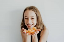 Crop positive Mädchen mit Sommersprossen lächelt und blickt in die Kamera, während sie Scheiben frischer gesunder Mandarine vorführt — Stockfoto