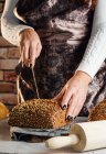 Ernte anonyme Bäckerin mit Messer schneidet Laib frisches Brot mit Sonnenblumenkernen auf Tisch in Backhaus — Stockfoto