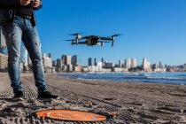 D'en haut de recadré mâle méconnaissable avec télécommande debout sur la plage avec drone placé sur la piste d'atterrissage — Photo de stock