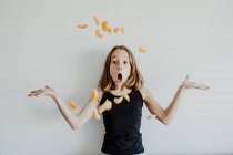 Amazed child in casual clothes throwing slices of mandarin and shrugging shoulders with opened mouth while having fun against white background — Stock Photo