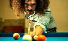 Crop focused bearded male hitting ball with cue while playing game in billiard pool — Stock Photo