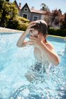 Fröhlicher, hemdloser kleiner Junge, der in den Sommerferien auf dem Land ins Pool-Wasser springt — Stockfoto