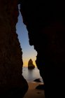 A través de la cueva rocosa de la pintoresca playa de arena del océano contra el cielo del atardecer en Praia do Camilo en Algarve, Portugal - foto de stock