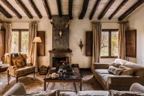 Geräumiges Wohnzimmer mit Sofa und weichen Kissen in der Nähe von Tisch und Kamin im Jagdhaus — Stockfoto