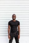 Conteúdo Homem afro-americano de t-shirt preta olhando para a câmera no fundo claro — Fotografia de Stock
