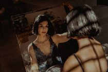 Мирная женщина сидит и смотрит на себя в прямоугольное зеркало на полу в комнате — стоковое фото