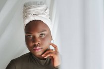 Portrait of alluring young black lady in casual clothes with turban and looking at camera — Stock Photo