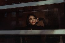 Через стекло вдумчивой женщины, стоящей у окна и смотрящей в сторону — стоковое фото