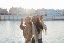 Seitenansicht von multirassischen Freundinnen mit Kopfhörern, die an sonnigen Tagen gemeinsam Musik genießen und auf einem Damm tanzen — Stockfoto