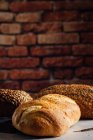 White and rye bread with cereals and appetizing crust on cutting board against brick wall in bakehouse — Stock Photo