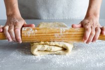 Crop unrecognizable female chef rolling out soft dough using wooden rolling pin with flour during cooking process in house — Stock Photo
