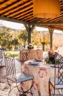 Amplia terraza con platos de viñas y cubiertos colocados en mesas decoradas con flores frescas para la celebración de la boda - foto de stock