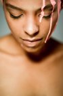 Modelo feminino étnico criativo com tinta rosa pingando em seu rosto olhando para baixo no fundo cinza em estúdio — Fotografia de Stock