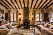 Geräumiges Wohnzimmer mit Sofa und weichen Kissen in der Nähe von Tisch und Kamin im Jagdhaus — Stockfoto