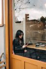 Dai capelli lunghi bruna asiatico donna avendo un caffè oh un caffè mentre è alla ricerca di un cellulare — Foto stock