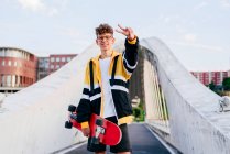 Adolescent caucasien debout avec une planche à roulettes au milieu du pont dans la ville — Photo de stock