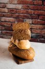 Куча белого и ржаного хлеба с зерновыми и аппетитной коркой на доске для резки на кирпичной стене в пекарне — стоковое фото