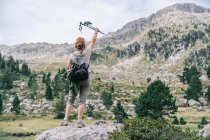 Погляд на анонімну жіночу туристку в повсякденному одязі з рюкзаком, який піднімає руку з скандинавськими піренеями, стоячи на кам'яній вершині пагорба в горах Руди в каталонських Піренеях. — стокове фото