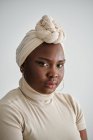 Linda jovem modelo feminino africano em elegante turbante tradicional em pé contra fundo branco e olhando para a câmera — Fotografia de Stock