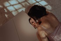 Hohe Winkel der zarten Frau im Nachthemd auf dem Boden liegend und reflektierend im Spiegel — Stockfoto