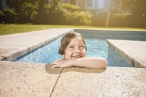 Niedliches lächelndes Kind lehnt am Beckenrand und ruht sich nach dem Schwimmen an einem sonnigen Tag aus — Stockfoto