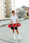 Bonito adolescente caucasiano com skate posando na rua — Fotografia de Stock