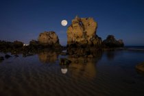 Scenic view of Arrifes Beach with rocky formations in pure rippled sea under cloudy sky with moon at night in Algarve Portugal — Stock Photo