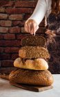 Panadero femenino anónimo de cosecha que muestra pan fresco suave con semillas crujientes en la mesa en la panadería - foto de stock