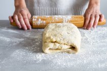 Crop unrecognizable female chef rolling out soft dough using wooden rolling pin with flour during cooking process in house — Stock Photo