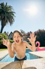 Lindo niño sonriente apoyado en el borde de la piscina mientras descansa después de nadar en un día soleado - foto de stock