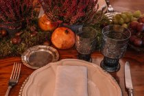 Angolo alto di bicchieri di cristallo vicino al piatto e posate poste sul tavolo decorate con uva Calluna vulgaris fiori e melograno — Foto stock