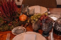 High angle of crystal glasses near plate and cutlery placed on table decorated with grapes Calluna vulgaris flowers and pomegranate — Stock Photo