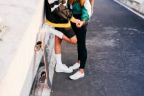 Cropped couple méconnaissable avec tenue urbaine et planche à roulettes couché sur un mur dans la rue — Photo de stock