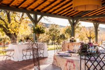Ampia veranda con piatti di bicchieri da vino e posate disposti su tavoli decorati con fiori freschi per la celebrazione del matrimonio — Foto stock